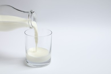 Pouring milk into glass on white background