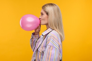 Photo of Woman blowing up balloon on yellow background