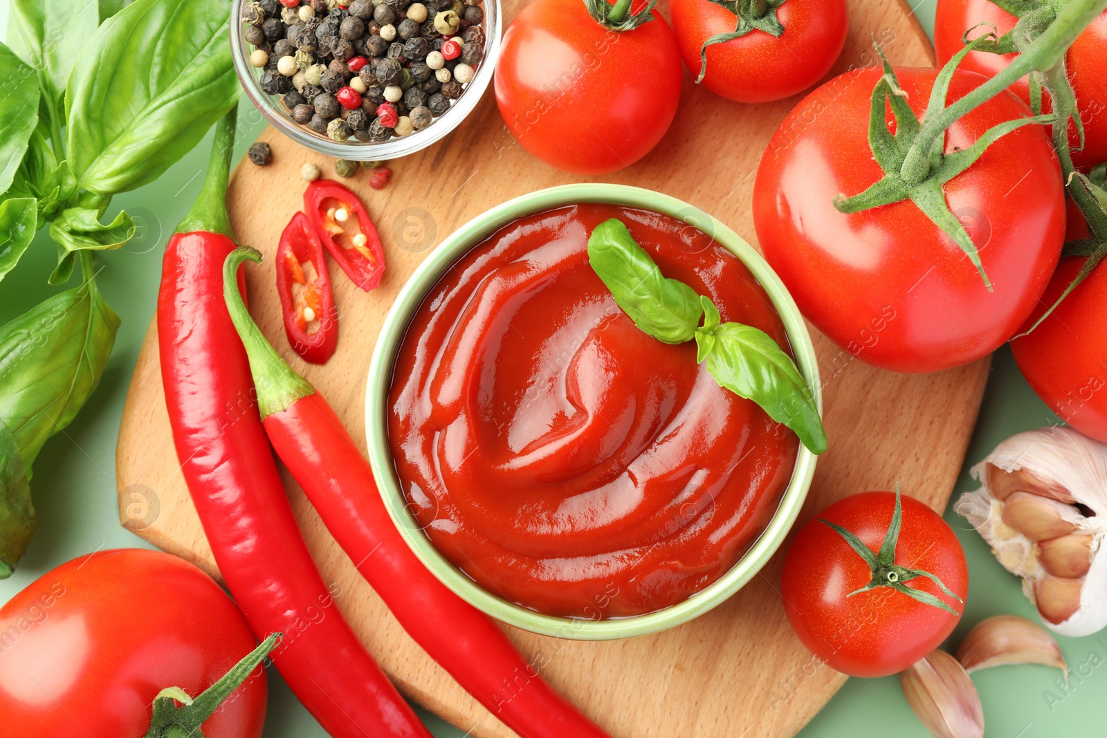 Photo of Bowl of tasty ketchup and ingredients on green table, flat lay