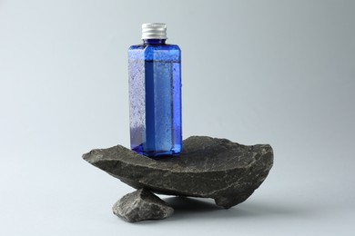 Photo of Bottle of cosmetic product on stones against light grey background
