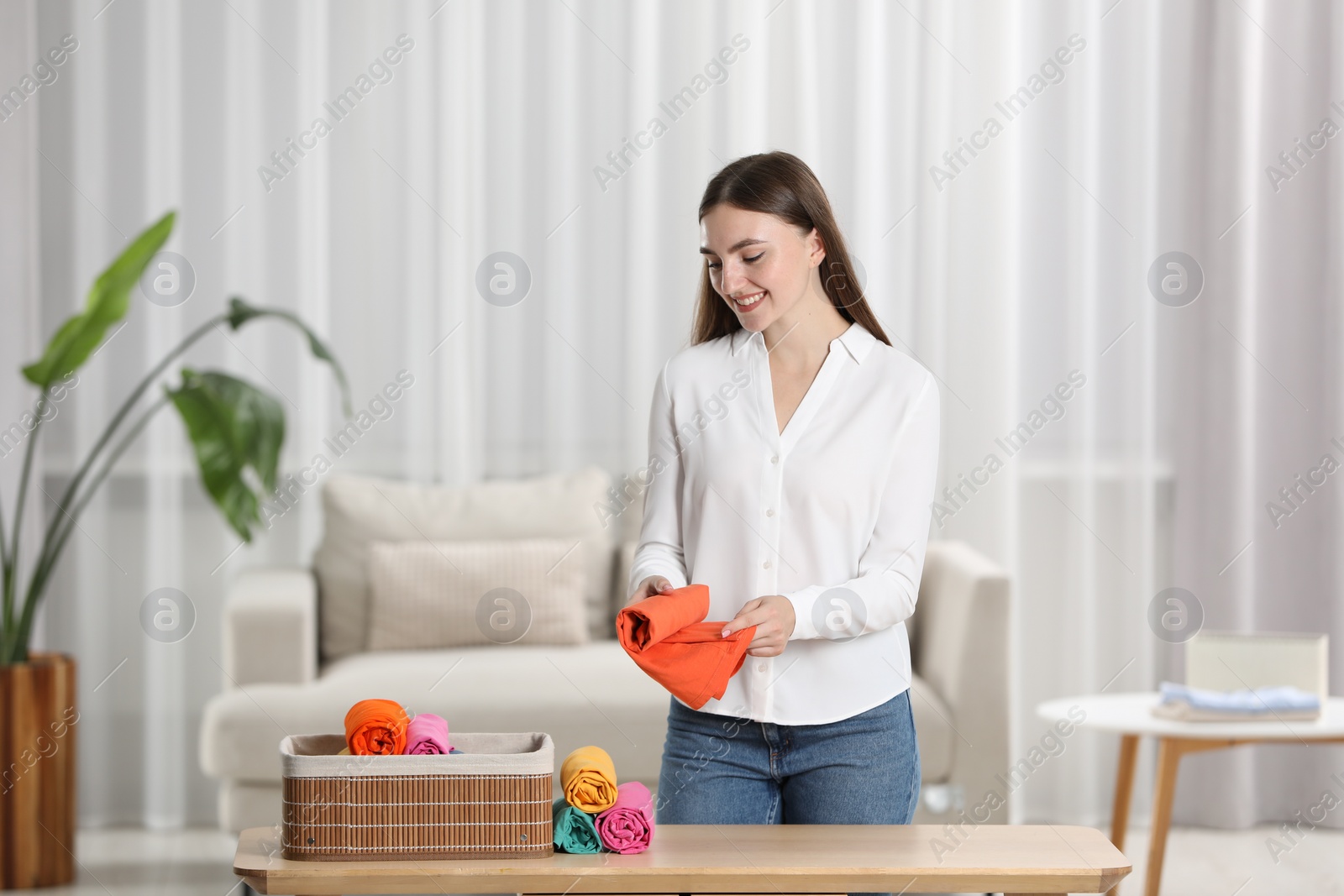 Photo of Smiling woman rolling shirt at table in room. Organizing clothes