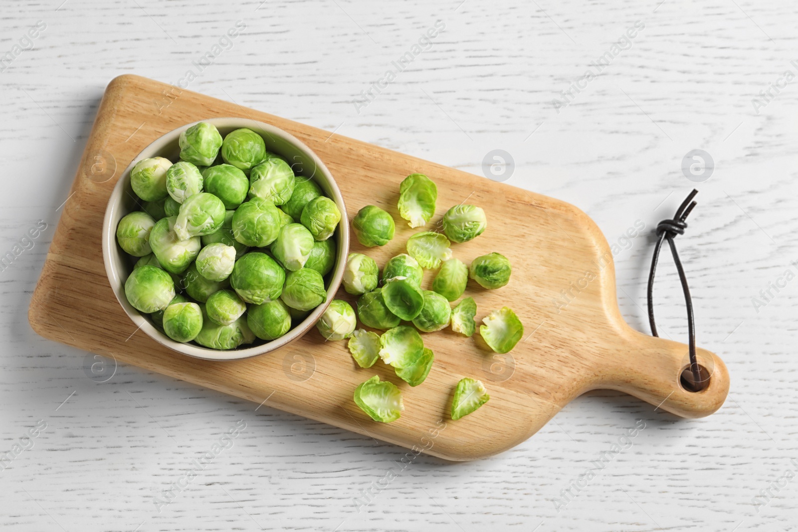 Photo of Board with bowl and Brussels sprouts on wooden background, top view