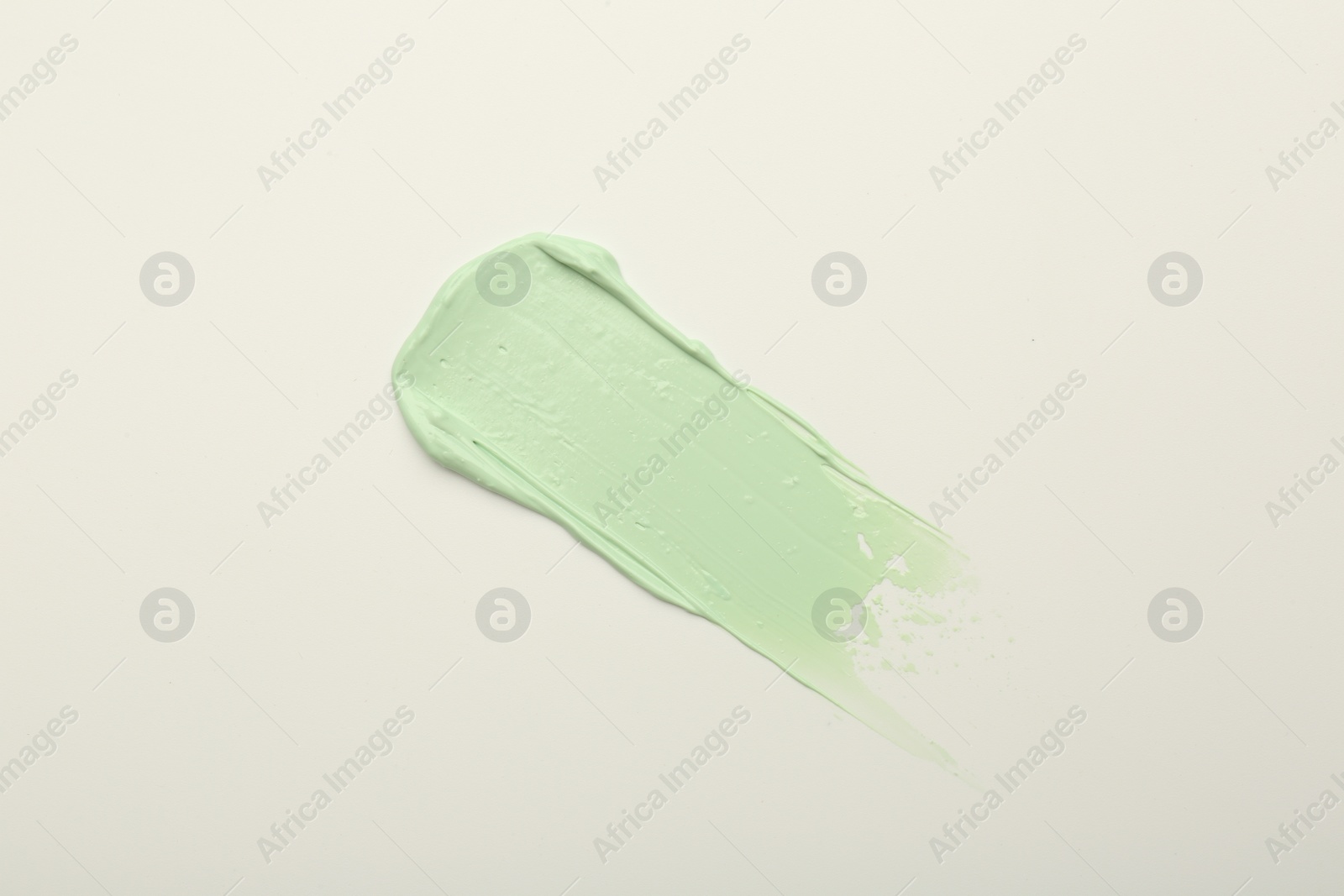 Photo of Stroke of green color correcting concealer on white background, top view