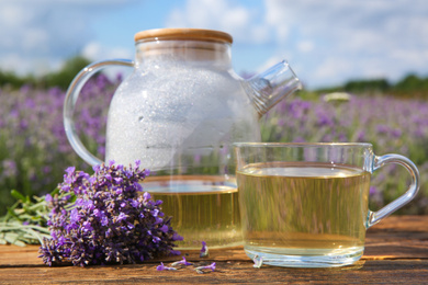 Photo of Tasty herbal tea and fresh lavender flowers on wooden table in field, closeup