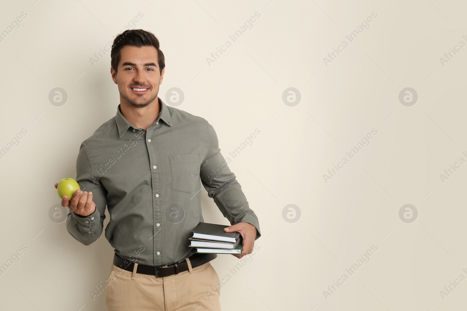 Photo of Young male teacher with books and apple on beige background. Space for text