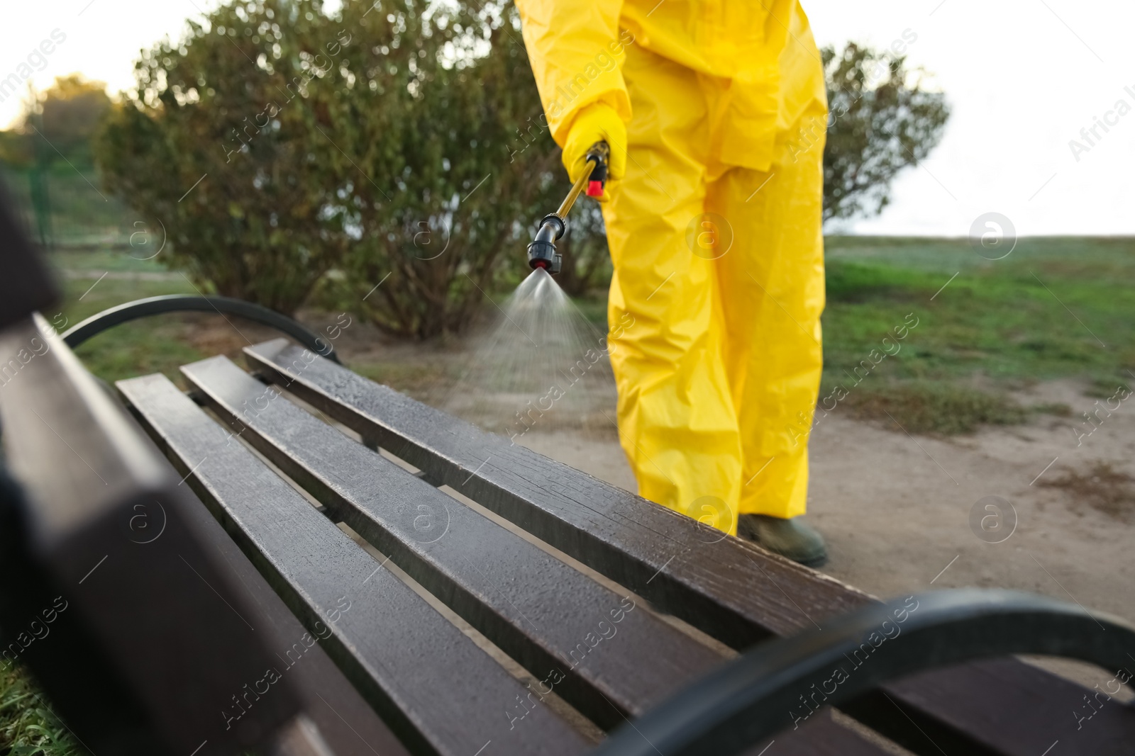 Photo of Person in hazmat suit disinfecting bench in park with sprayer, closeup. Surface treatment during coronavirus pandemic