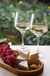 Glasses of white wine and snacks served on wooden table outdoors