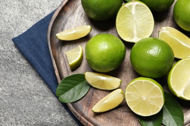 Photo of Fresh ripe limes and leaves on grey table, top view