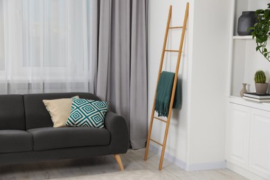 Photo of Wooden ladder near shelving unit and sofa in room