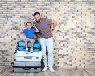 Photo of Man and his son with suitcases near brick wall. Vacation travel