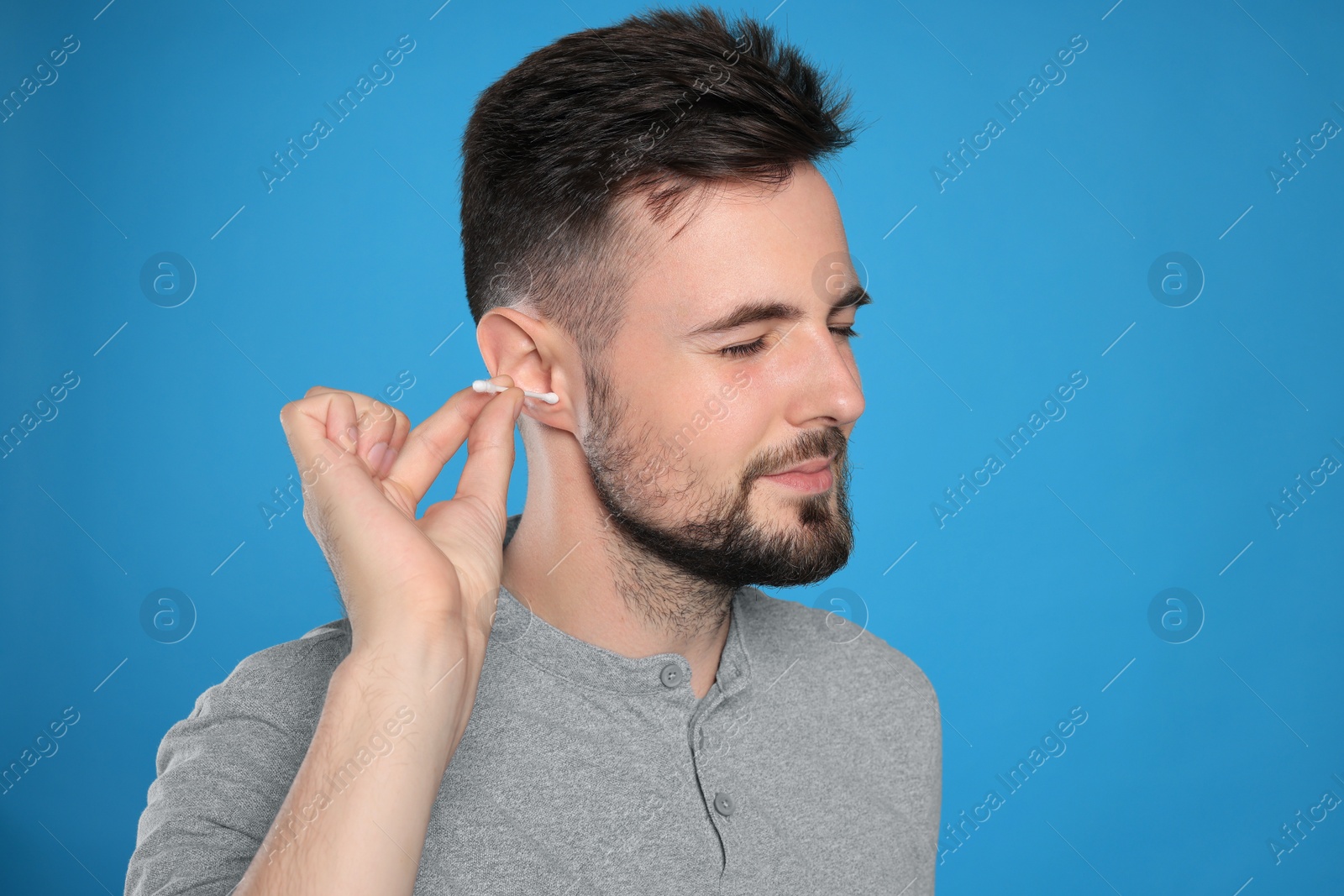 Photo of Young man cleaning ear with cotton swab on light blue background