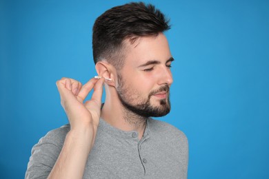 Young man cleaning ear with cotton swab on light blue background