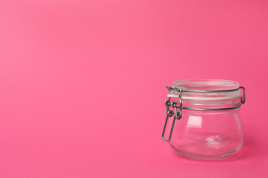 Closed empty glass jar on pink background, space for text