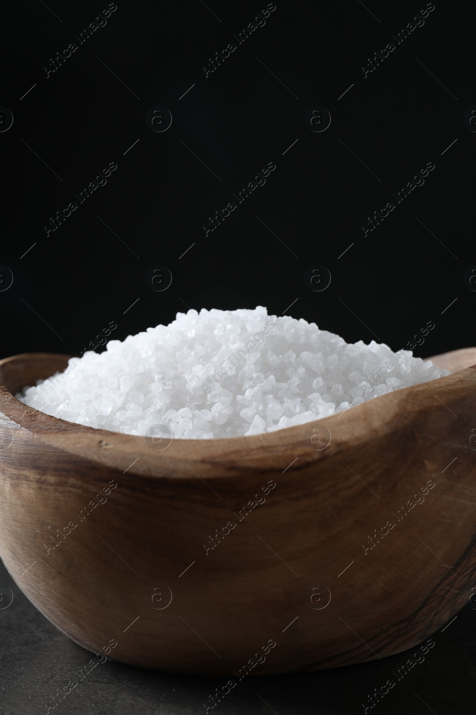 Photo of Natural salt in wooden bowl on dark grey table, closeup