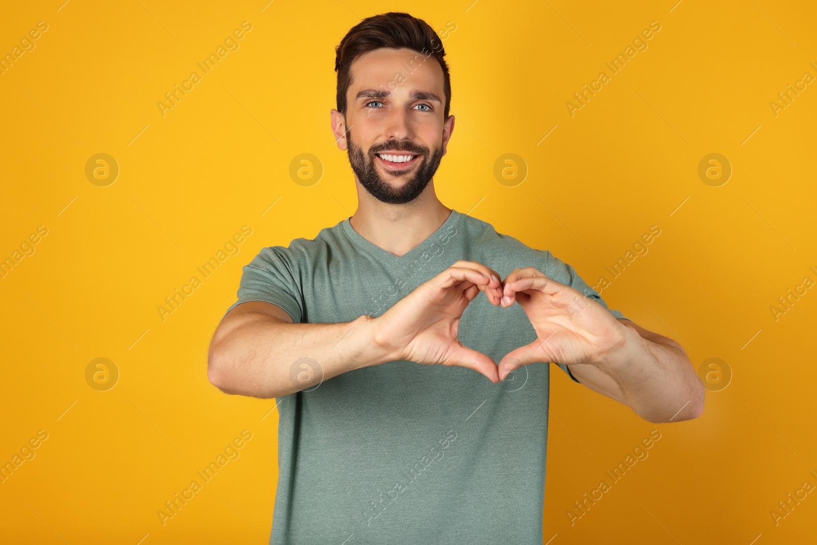 Photo of Happy man making heart with hands on yellow background