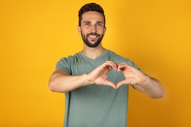 Photo of Happy man making heart with hands on yellow background