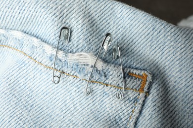 Metal safety pins on denim fabric, closeup