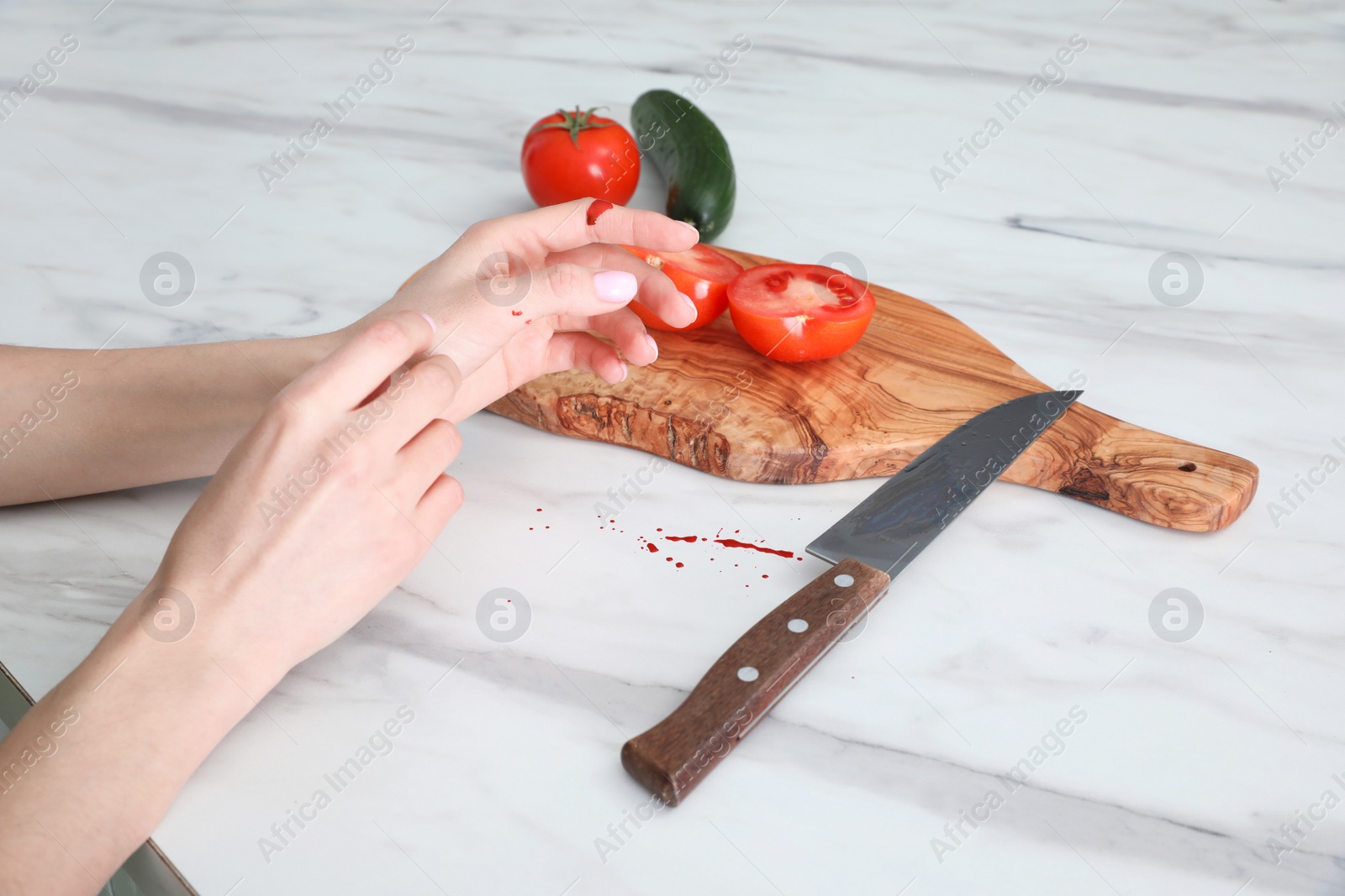 Photo of Young woman cutting finger with knife while cooking at white marble table, closeup