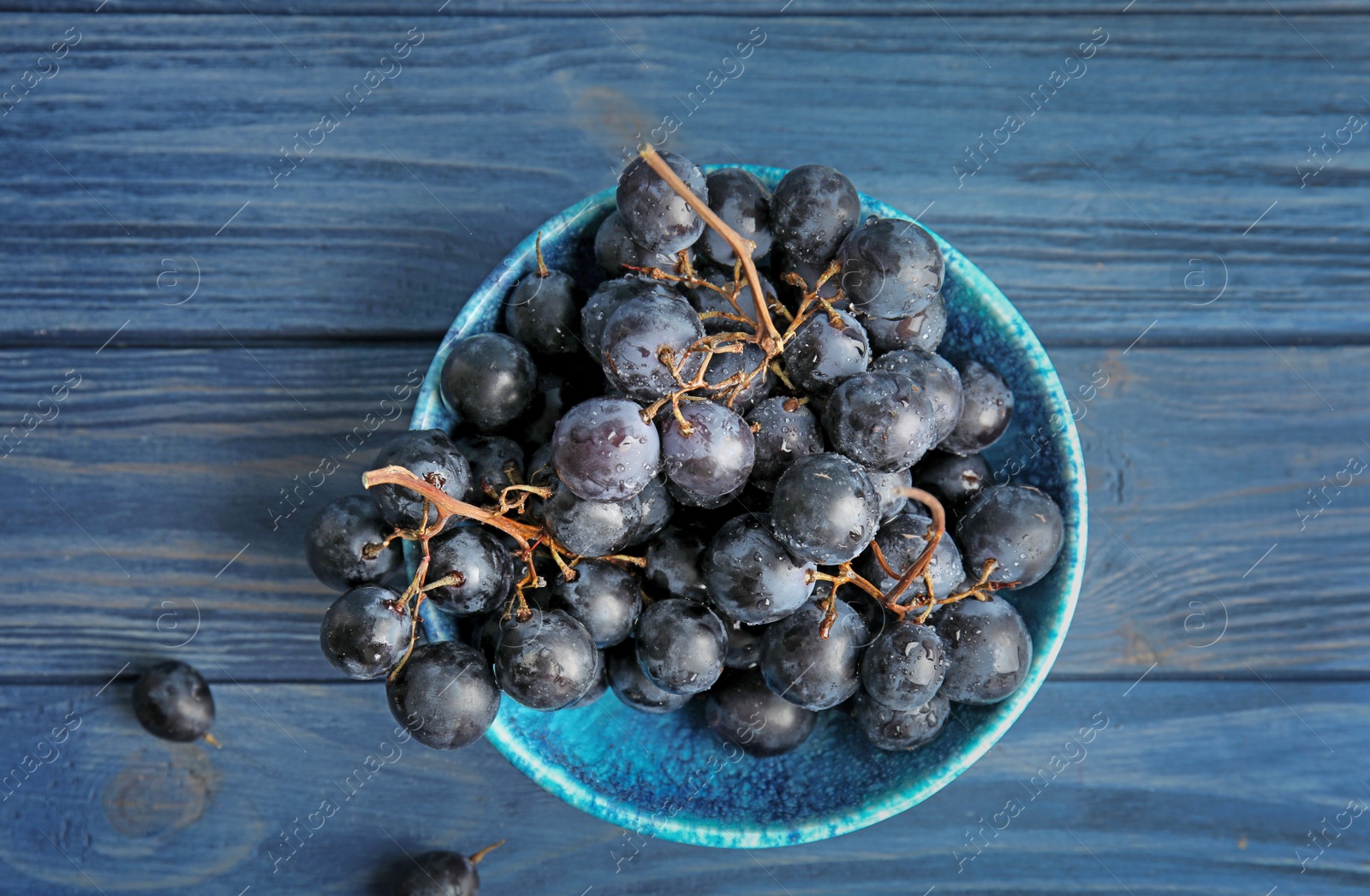 Photo of Fresh ripe juicy grapes in bowl on wooden background, top view