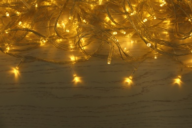 Glowing Christmas lights on white wooden background, top view