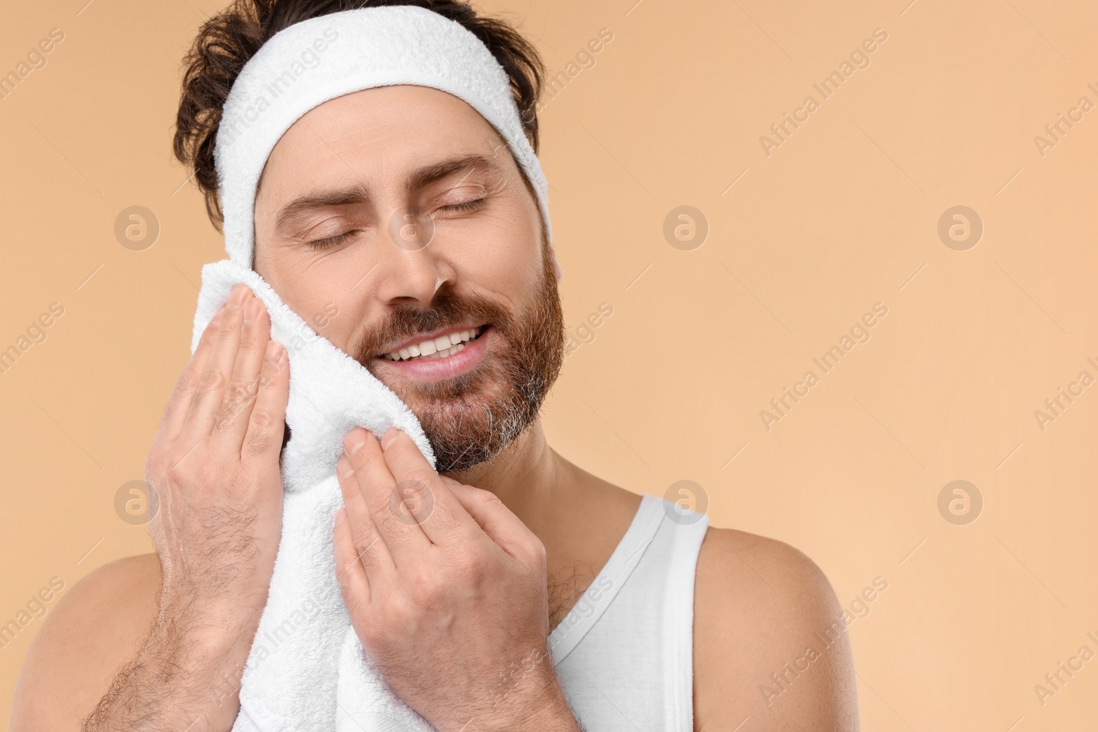 Photo of Washing face. Man with headband and towel on beige background, space for text