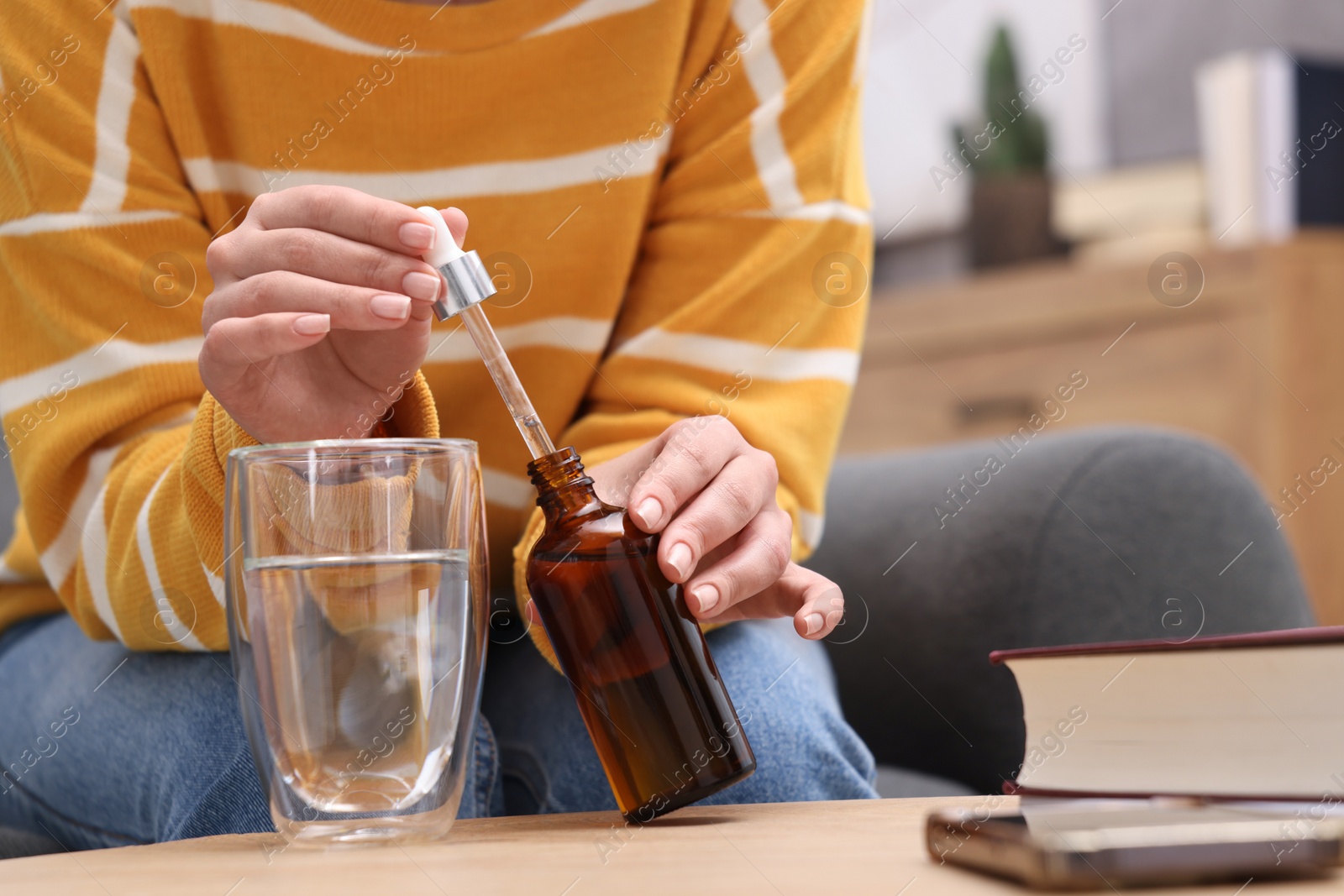 Photo of Woman dripping food supplement into glass of water on wooden table indoors, closeup