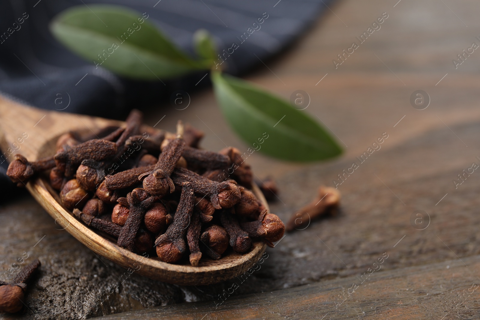 Photo of Spoon with aromatic cloves on wooden table, closeup. Space for text