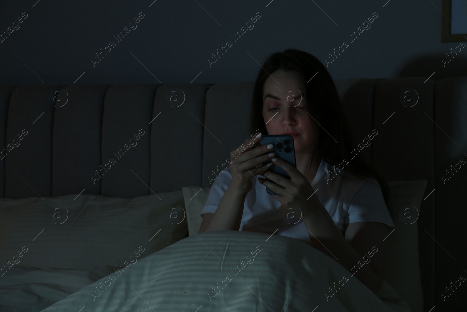 Photo of Woman using smartphone in bed at night. Internet addiction