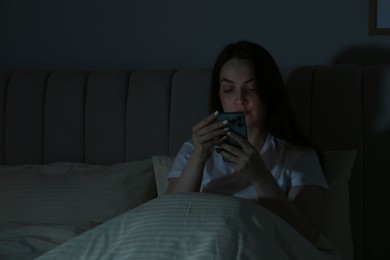 Photo of Woman using smartphone in bed at night. Internet addiction