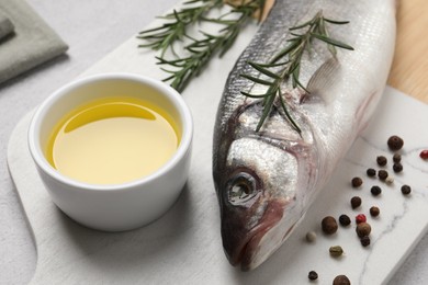 Photo of Sea bass fish and ingredients on light grey table, closeup