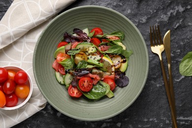 Delicious vegetable salad served on black textured table, flat lay