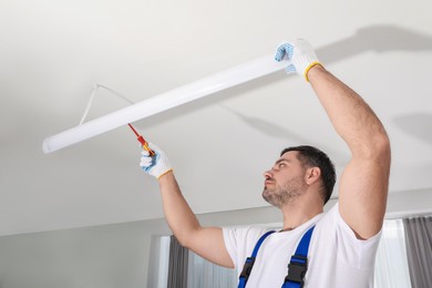 Electrician installing led linear lamp indoors. Ceiling light