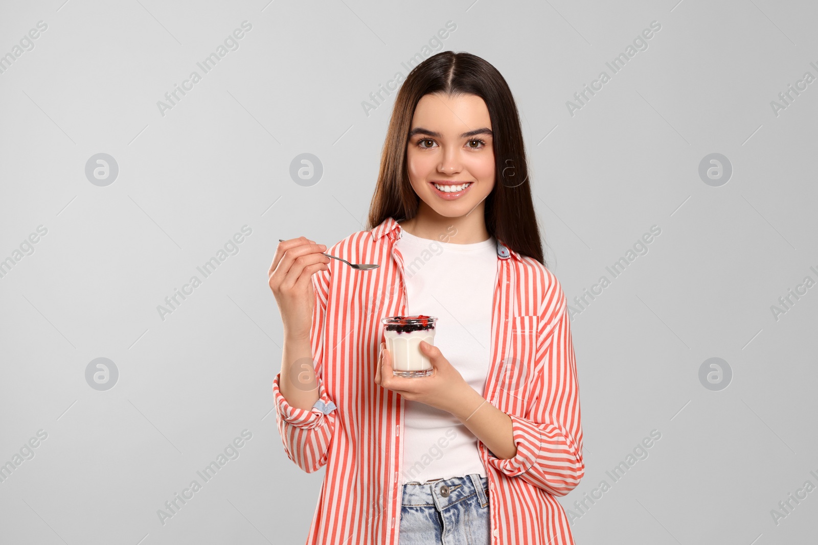 Photo of Happy teenage girl with delicious yogurt and spoon on light grey background