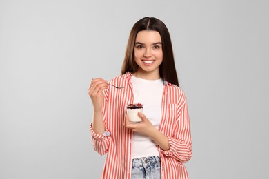 Happy teenage girl with delicious yogurt and spoon on light grey background