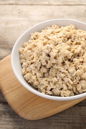 Photo of Tasty boiled oatmeal in bowl on wooden table