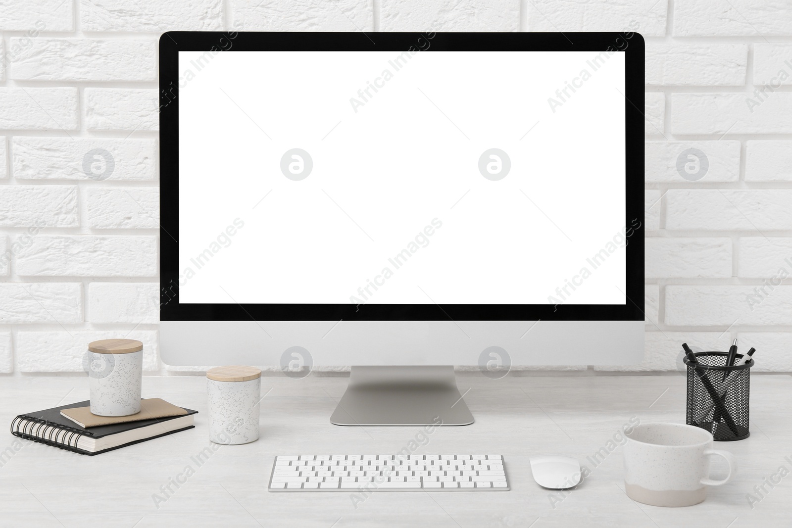 Photo of Office workplace with computer, cup and stationery on light table near white brick wall