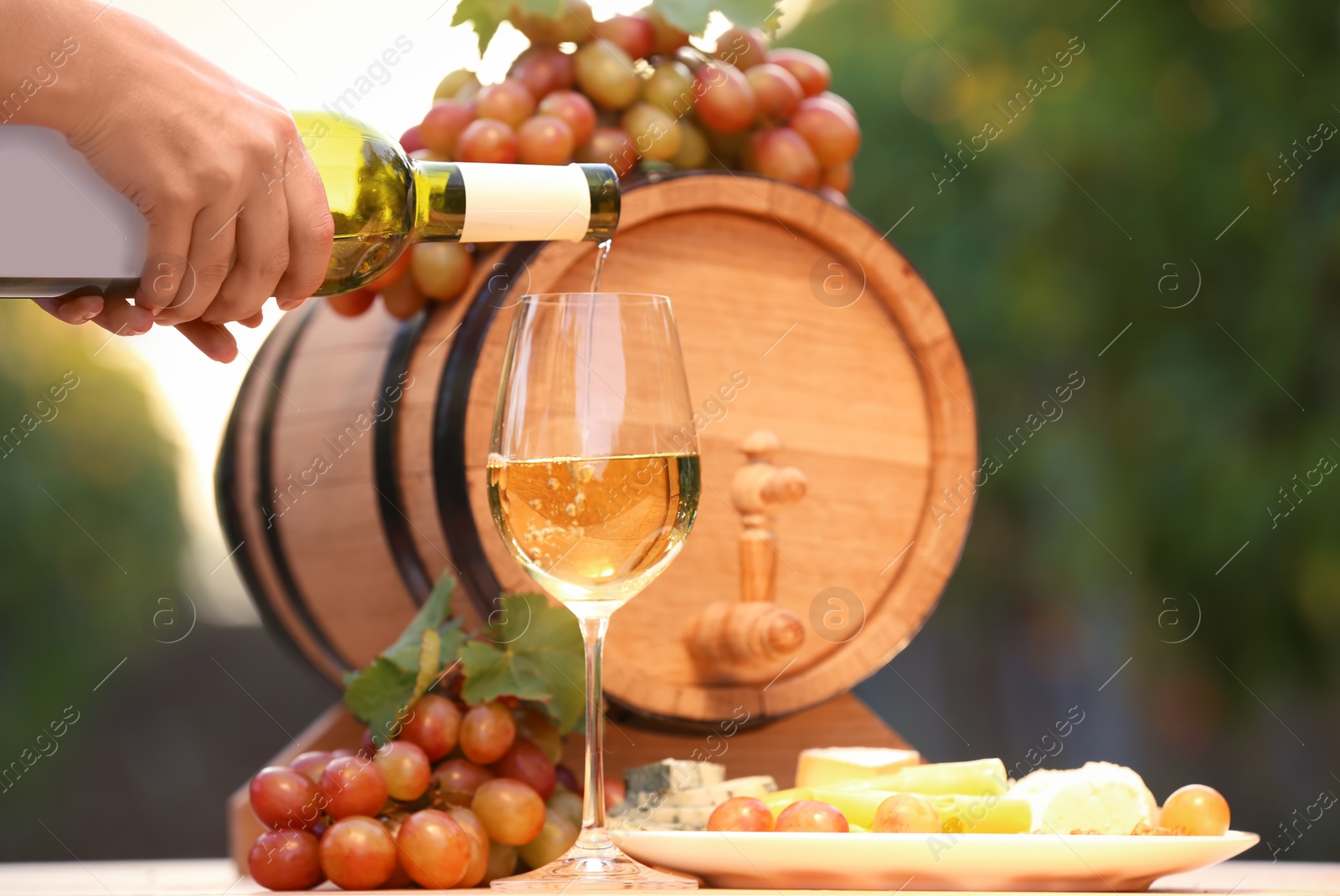 Photo of Woman pouring white wine into glass on table outdoors