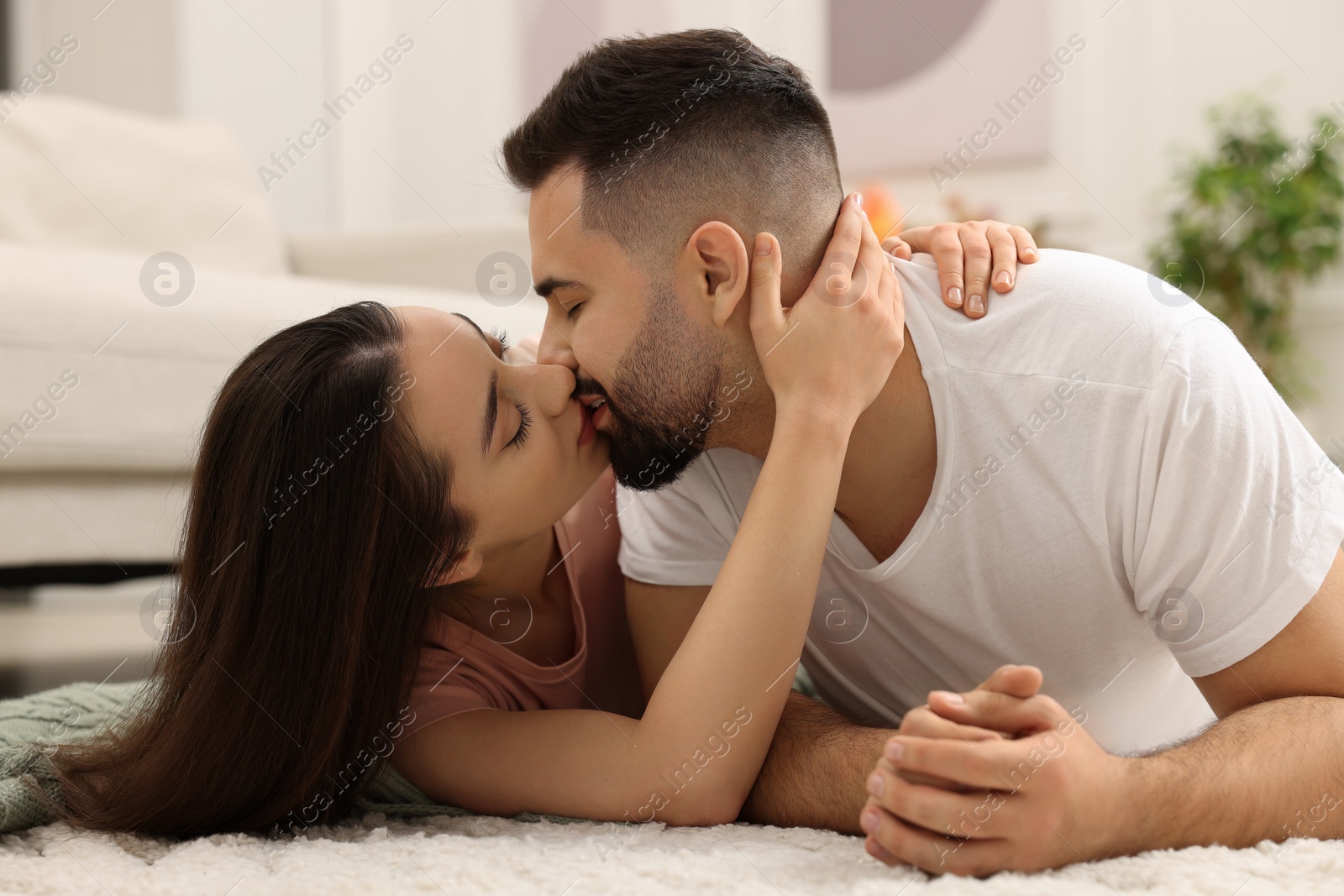 Photo of Affectionate young couple kissing on soft carpet at home