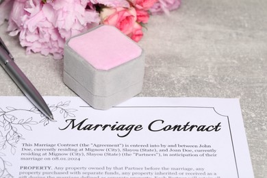 Photo of Marriage contract, pen, jewelry box and flowers on grey table, closeup