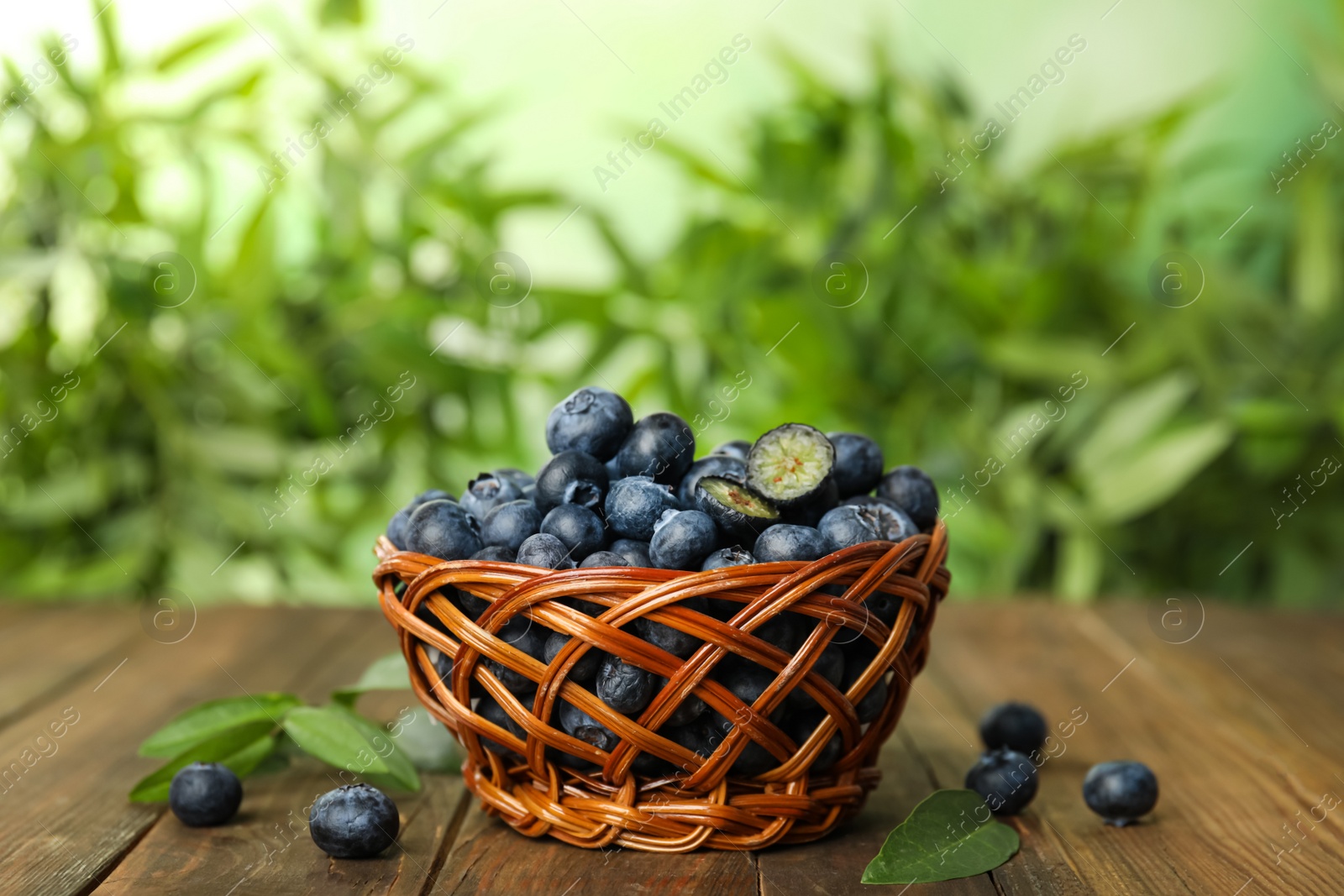 Photo of Tasty ripe blueberries in wicker bowl on wooden table