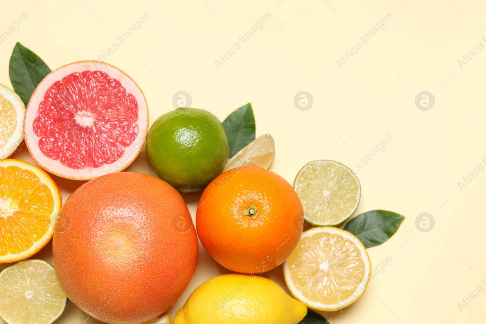 Photo of Different cut citrus fruits and leaves on beige table, flat lay. Space for text