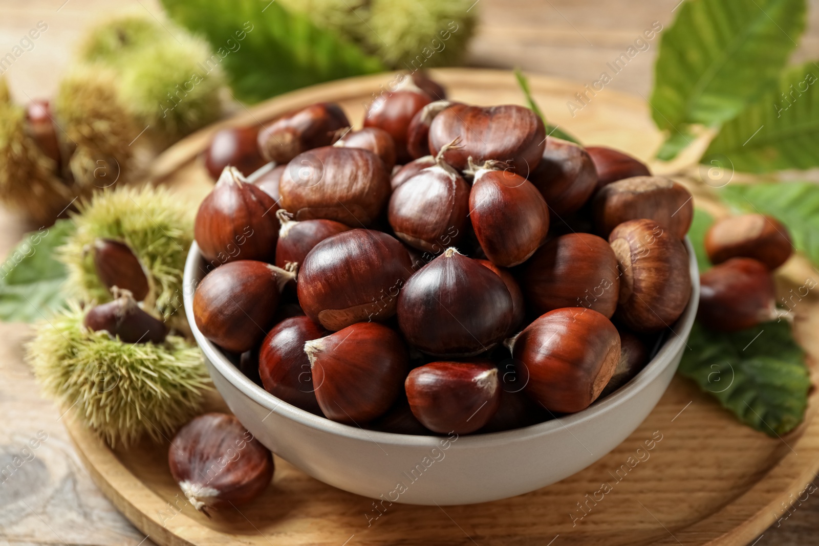 Photo of Fresh sweet edible chestnuts in bowl on wooden board
