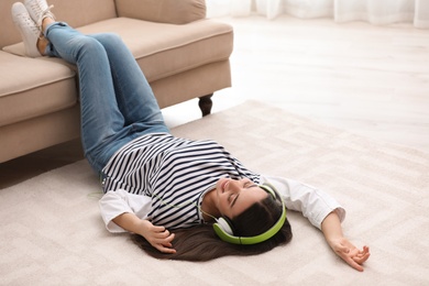 Young woman with headphones listening to music on floor in living room