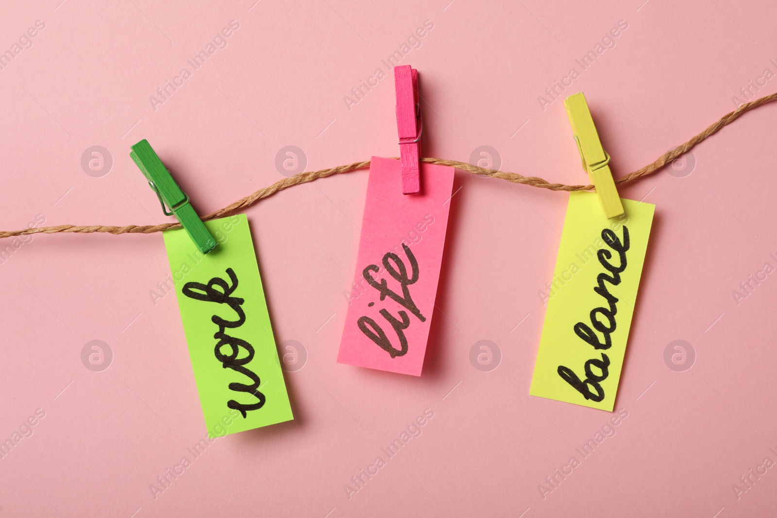 Photo of Paper pieces with words Work, Life, Balance hanging on rope against pink background, flat lay