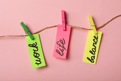 Paper pieces with words Work, Life, Balance hanging on rope against pink background, flat lay