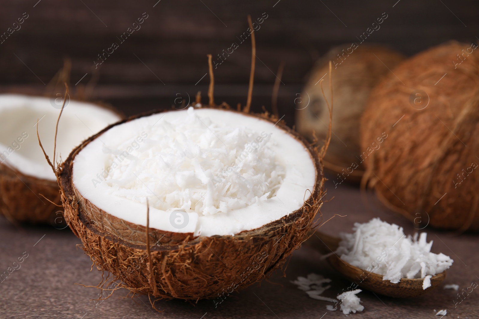 Photo of Coconut flakes in nut shell and spoon on brown table, closeup