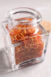 Aromatic saffron and glass jar on light gray table, closeup