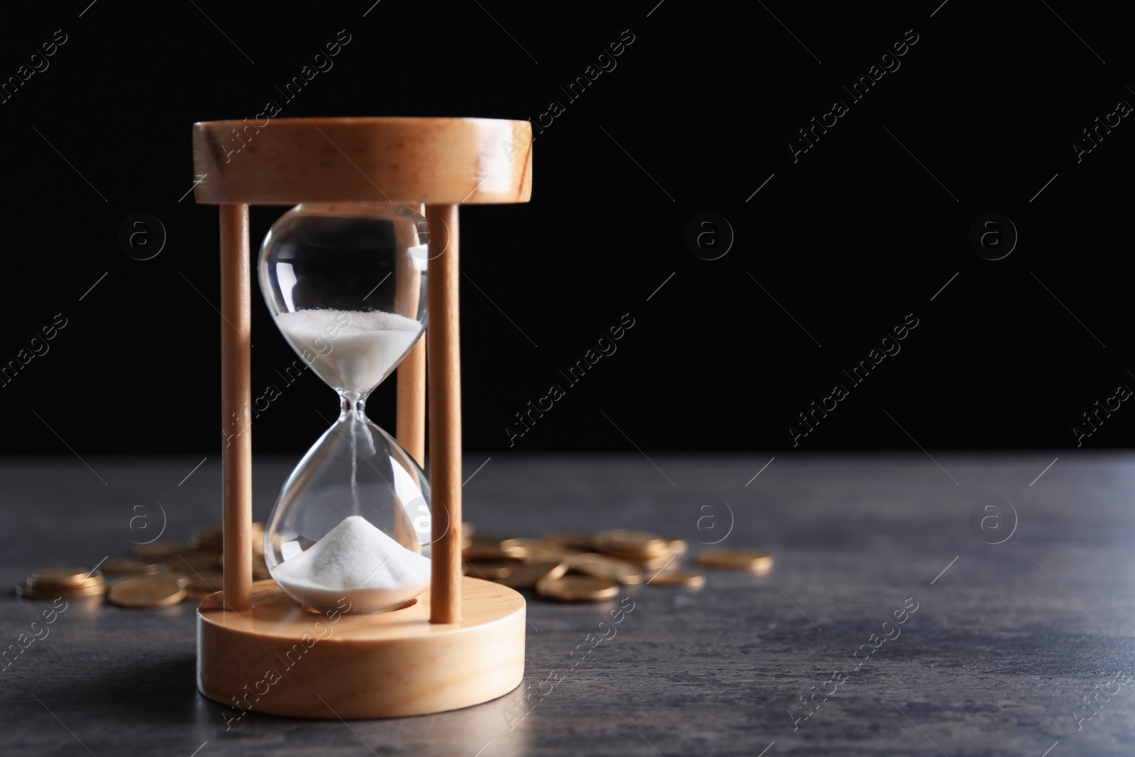 Photo of Hourglass and coins on table against black background. Time management
