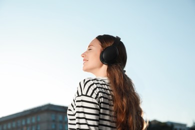 Photo of Smiling woman in headphones listening to music outdoors