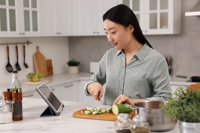 Photo of Beautiful woman looking at recipe on tablet while cooking in kitchen